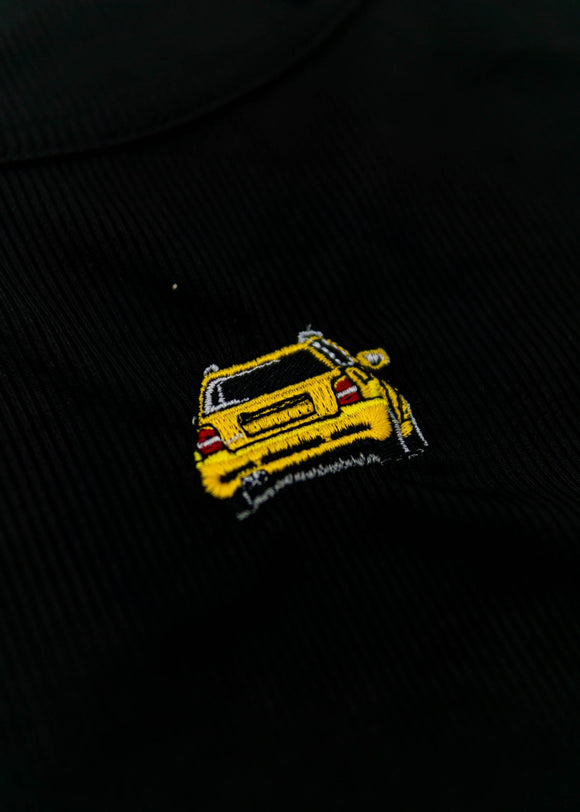 A black Audi crop top for women. Photo is a close up view of the top with an embroidered imola yellow Audi B5 RS4. Fabric composition is polyester, and elastine. The material is stretchy, ribbed, and non-transparent. The style of this shirt is sleeveless, with a crewneck neckline.