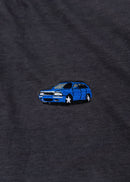 A dark grey cropped t-shirt for Audi women. Close up view of a 100% cotton crop tee with an embroidered Nogaro Blue Audi 80 RS2 Avant made by Porsche. The material is stretchy, and non-transparent with a crewneck neckline and short sleeves.