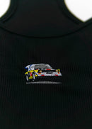 A black Audi crop top for women. Photo is a close up view of the top with an embroidered Audi Sport Quattro S1 E2. Fabric composition is polyester, and cotton. The material is stretchy, ribbed, and non-transparent. The style of this shirt is sleeveless, with a scoop neckline.