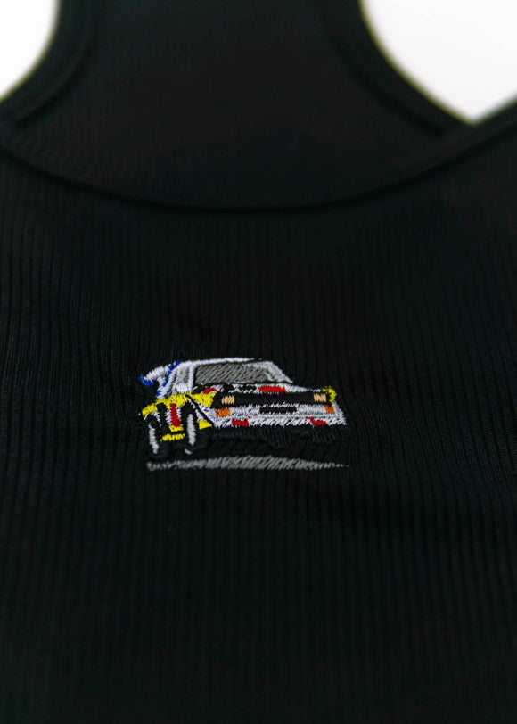 A black Audi crop top for women. Photo is a close up view of the top with an embroidered Audi Sport Quattro S1 E2. Fabric composition is polyester, and cotton. The material is stretchy, ribbed, and non-transparent. The style of this shirt is sleeveless, with a scoop neckline.