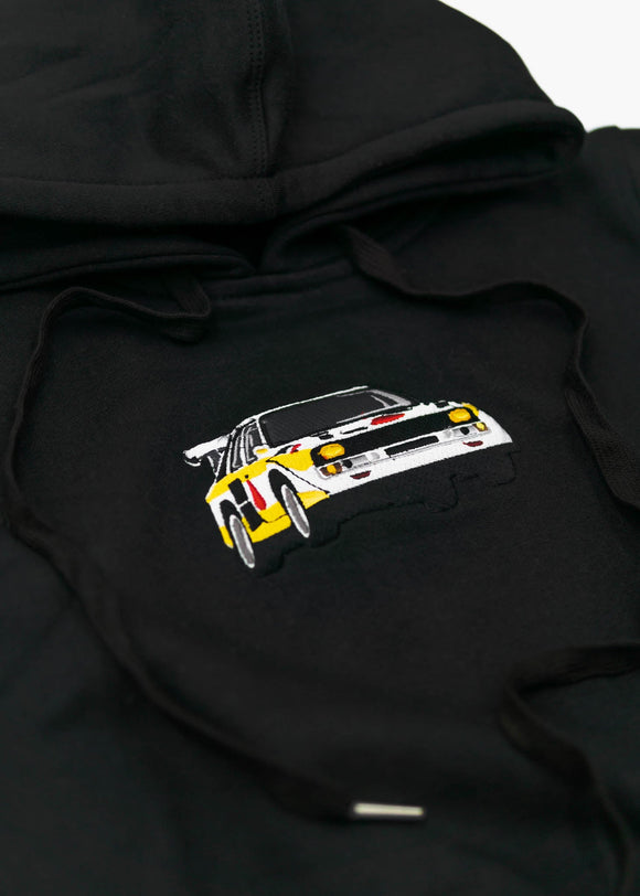 A black Audi cropped hoodie for women. Photo is a front view of the cropped sweater with an embroidered Sport Quattro S1 E2. Fabric composition is cotton, and polyester. The material is soft, stretchy, and non-transparent. The style of this crop hoodie is long sleeve, crewneck with a hood, hooded, with embroidery on the chest.