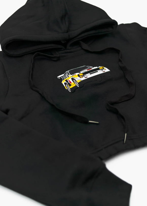 A black Audi cropped hoodie for women. Photo is a front view of the cropped sweater with an embroidered Sport Quattro S1 E2. Fabric composition is cotton, and polyester. The material is soft, stretchy, and non-transparent. The style of this crop hoodie is long sleeve, crewneck with a hood, hooded, with embroidery on the chest.