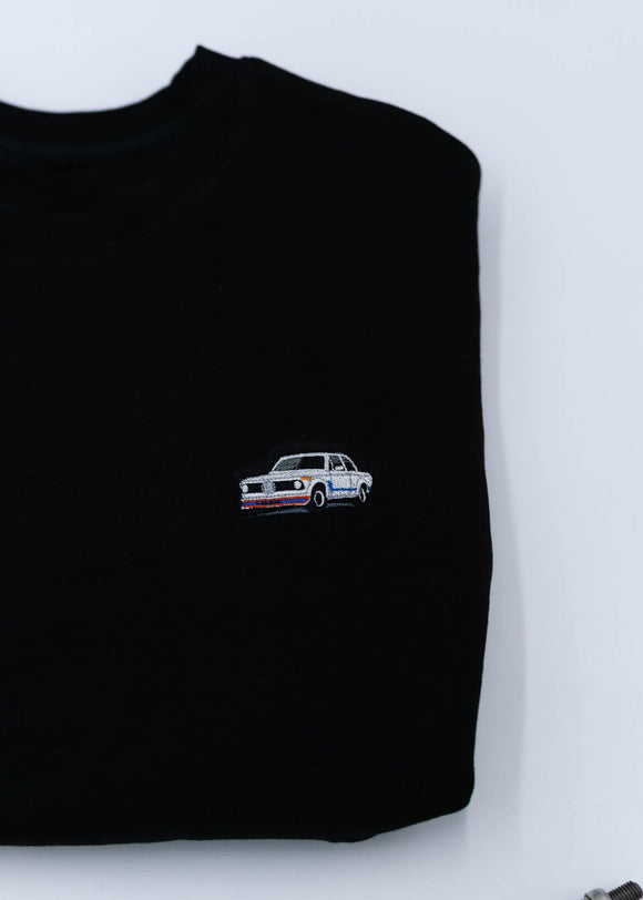 A black BMW crewneck sweater for men. Photo is a close up of the sweater with an embroidered BMW 2002 Turbo. Fabric is composed of high quality 80% cotton, and 20% polyester and fits to size. The style is long sleeve, crew neck, and embroidery on left chest.