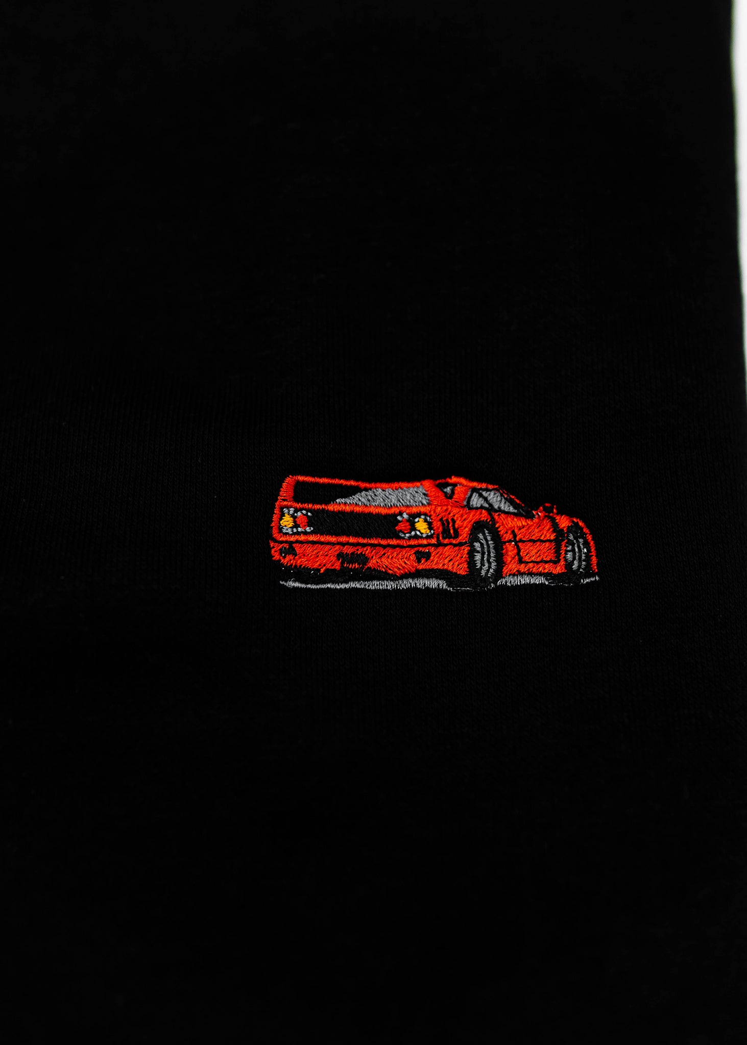 Close up of an embroidered F40 on a black men's high quality crewneck sweater. Photo shows the high quality detailed embroidery of a red F40. Fabric composition of the shirt is cotton and polyester. The material is very soft, stretchy, and non-transparent. The style of this sweater is a crewneck, long sleeve, elastic bottom, with embroidery on the left chest.