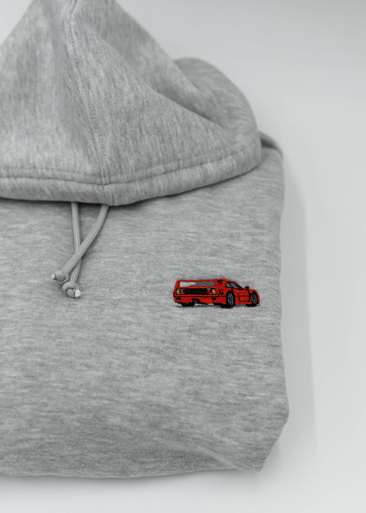 Close up of an embroidered F40 on a women's high quality cropped grey hoodie. Photo shows the detailed embroidery of a red F40. Fabric composition of this cropped sweater is polyester and cotton. The material is very soft, stretchy, and non-transparent. The style of this crop hoodie is a crewneck, drawstring hoodie, hooded, long sleeve, cropped, with embroidery on the left chest.