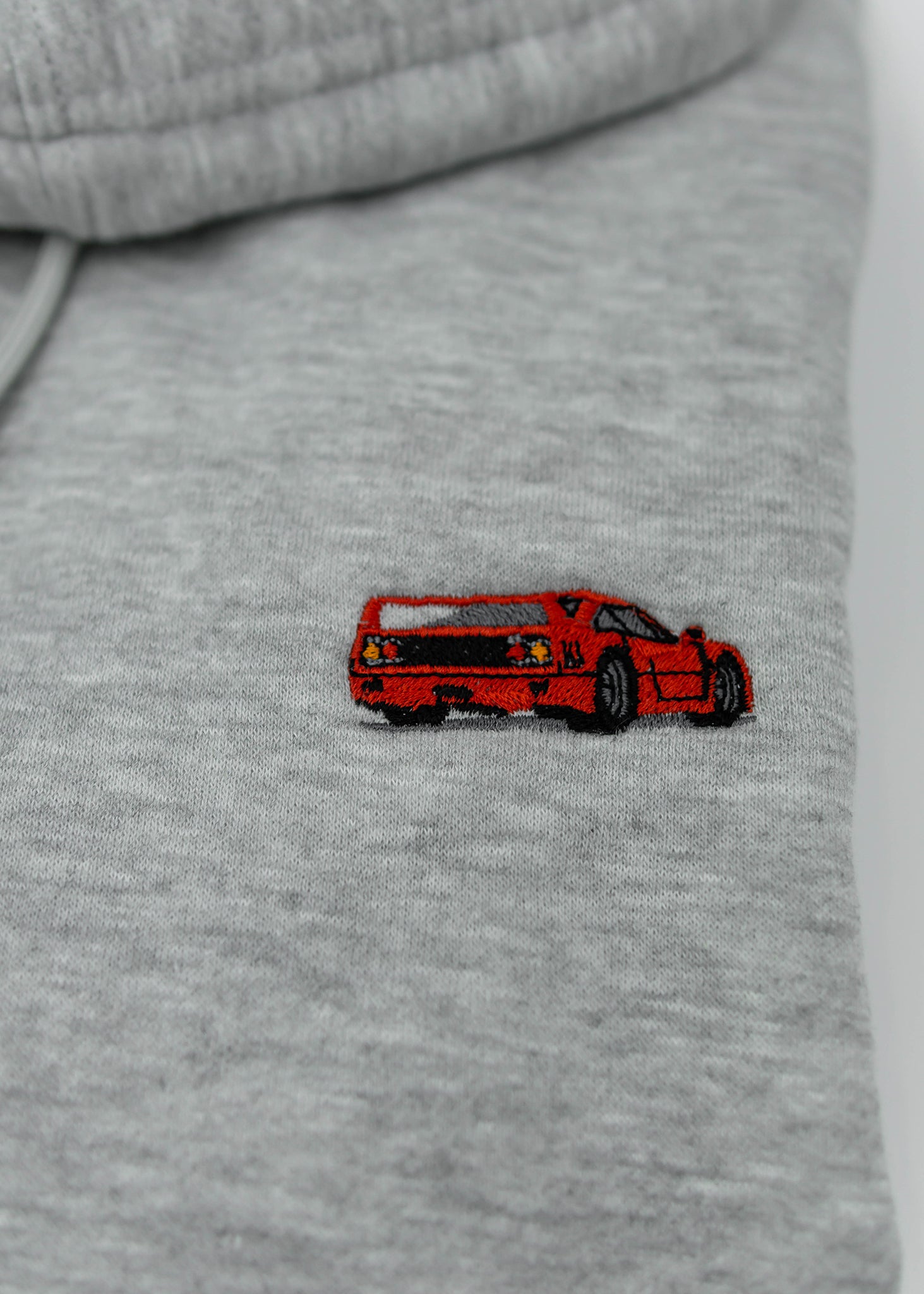 Close up of an embroidered F40 on a women's high quality cropped grey hoodie. Photo shows the detailed embroidery of a red F40. Fabric composition of this cropped sweater is polyester and cotton. The material is very soft, stretchy, and non-transparent. The style of this crop hoodie is a crewneck, drawstring hoodie, hooded, long sleeve, cropped, with embroidery on the left chest.