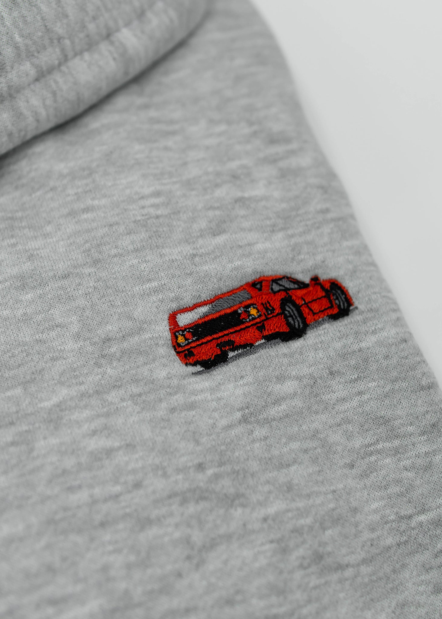 Close up of an embroidered F40 on a women's high quality cropped grey hoodie. Photo shows the detailed embroidery of a red F40. Fabric composition of this cropped sweater is polyester and cotton. The material is very soft, stretchy, and non-transparent. The style of this crop hoodie is a crewneck, drawstring hoodie, hooded, long sleeve, cropped, with embroidery on the left chest.