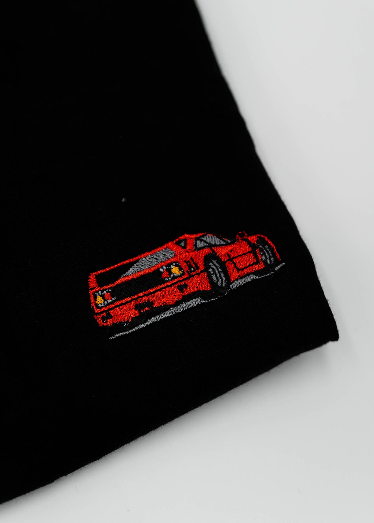 Close up of an embroidered F40 on a women's high quality cropped t-shirt. Photo shows the detailed embroidery of a red F40. Fabric composition of this tee is 100% cotton. The material is very soft, stretchy, and non-transparent. The style of this tshirt is a crewneck, short sleeve, cropped at the waist, with embroidery on the left chest.