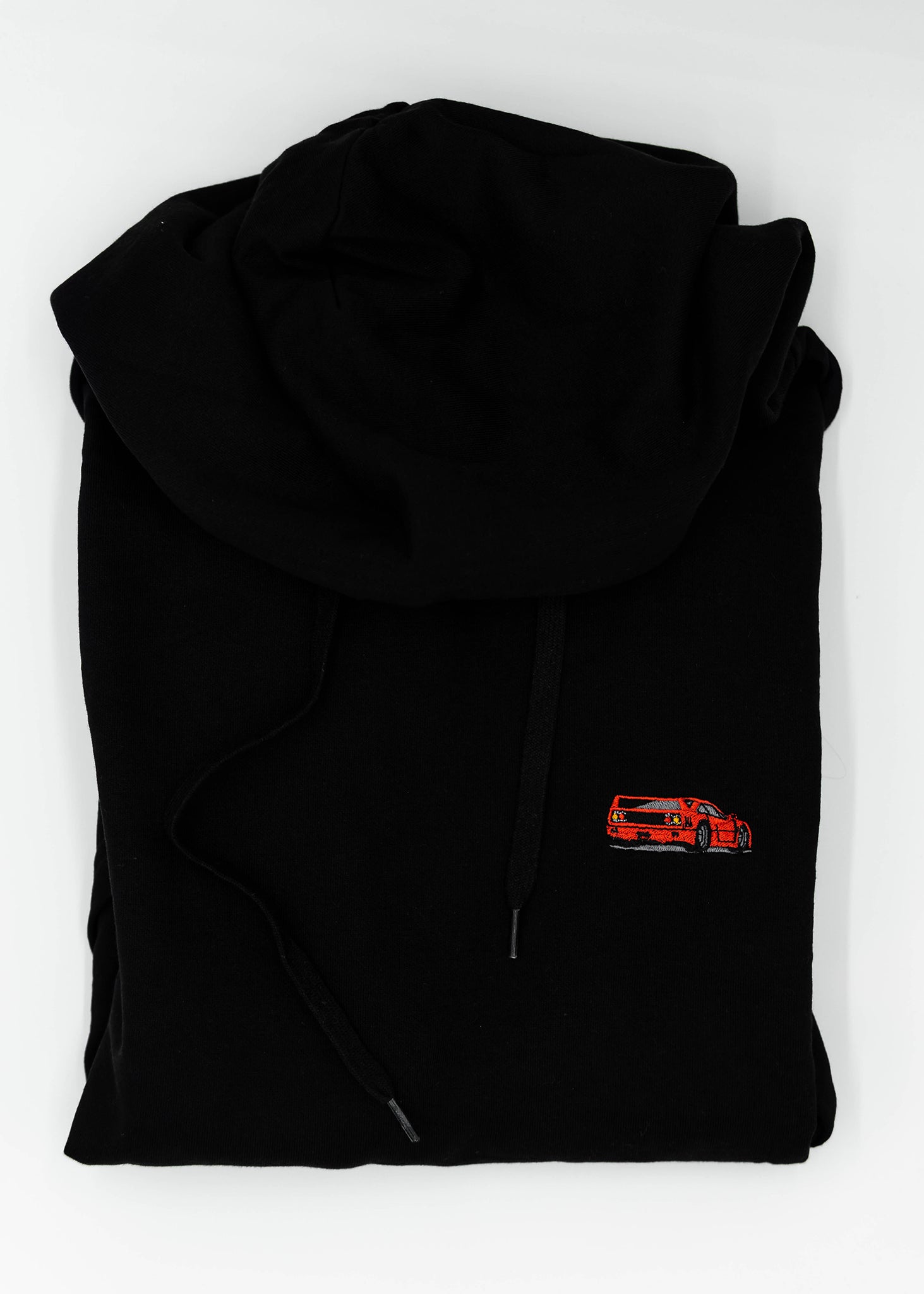 Close up of an embroidered F40 on a black unisex hoodie for men and women. Photo shows the high quality detailed embroidery of a red F40. Fabric composition of the sweater is cotton, polyester, and rayon. The material is very soft, stretchy, and non-transparent. The style of this hoodie is long sleeve, crewneck with a hood, hooded, with embroidery on the left chest.