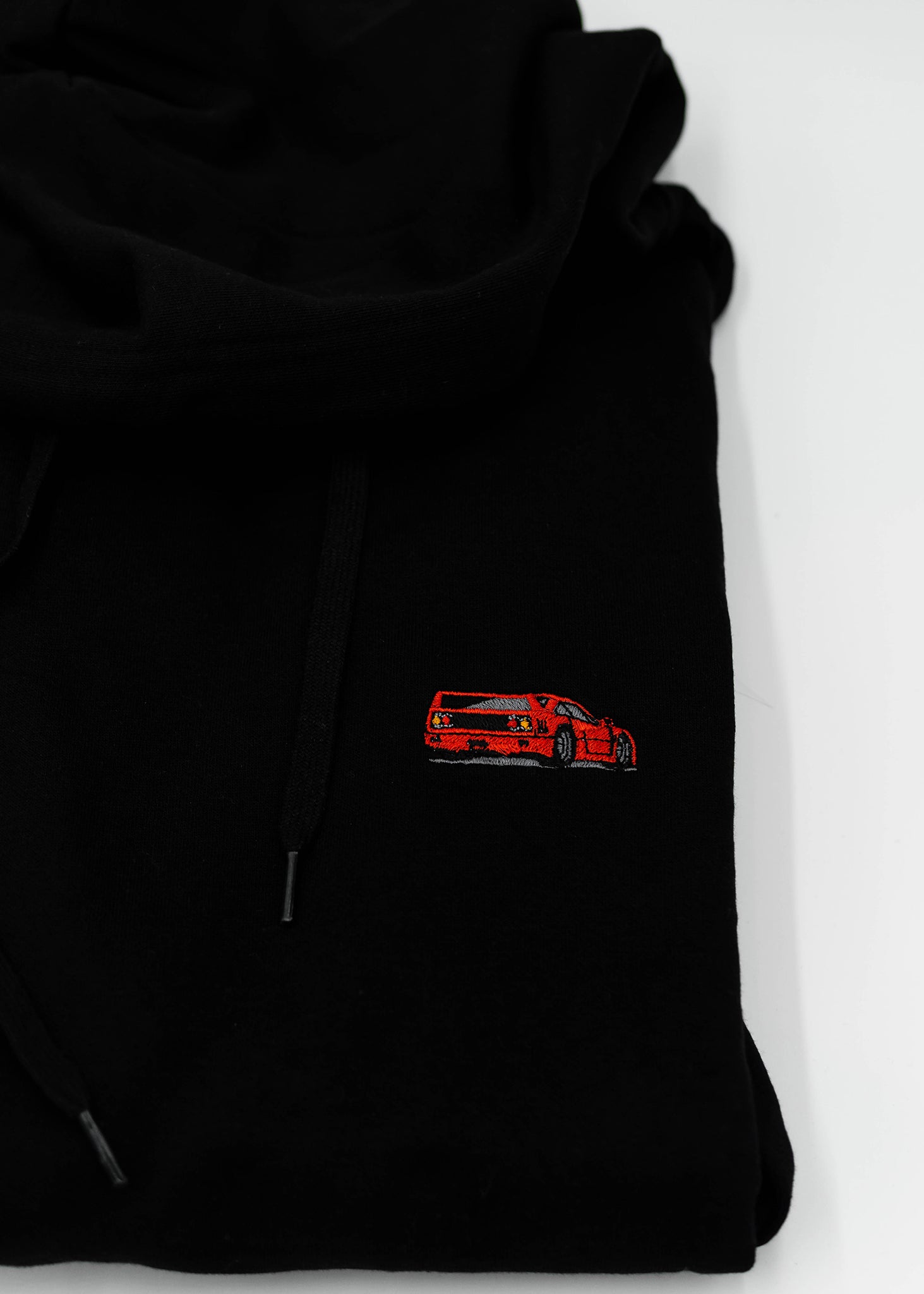 Close up of an embroidered F40 on a black unisex hoodie for men and women. Photo shows the high quality detailed embroidery of a red F40. Fabric composition of the sweater is cotton, polyester, and rayon. The material is very soft, stretchy, and non-transparent. The style of this hoodie is long sleeve, crewneck with a hood, hooded, with embroidery on the left chest.