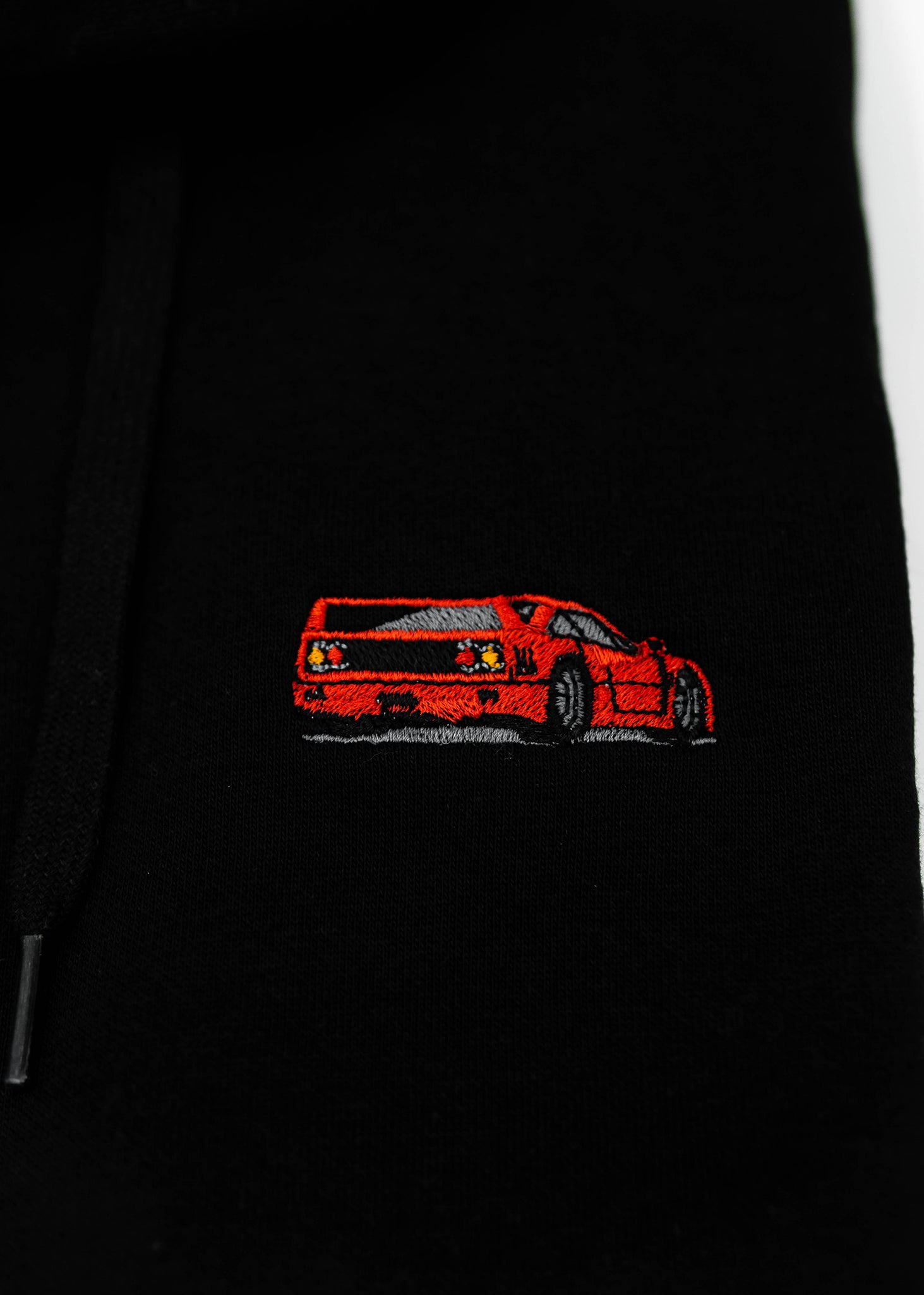 Close up of an embroidered F40 on a black unisex hoodie for men and women. Photo shows the high quality detailed embroidery of a red F40. Fabric composition of the sweater is cotton, polyester, and rayon. The material is very soft, stretchy, and non-transparent. The style of this hoodie is long sleeve, crewneck with a hood, hooded, with embroidery on the left chest.
