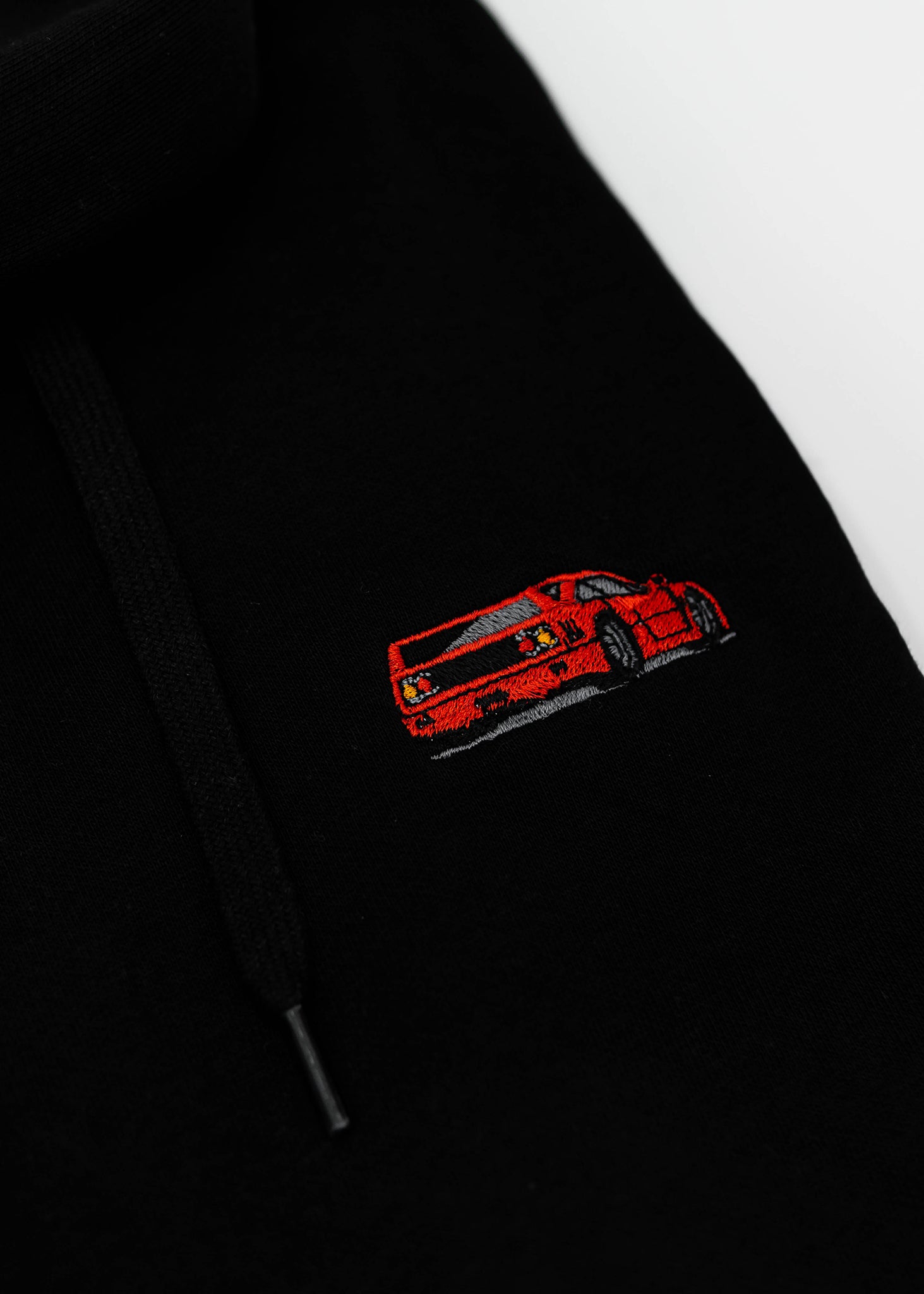 Close up of an embroidered F40 on a black unisex hoodie for men and women. Photo shows the high quality detailed embroidery of a red F40. Fabric composition of the sweater is cotton, polyester, and rayon. The material is very soft, stretchy, and non-transparent. The style of this hoodie is long sleeve, crewneck with a hood, hooded, with embroidery on the left chest.