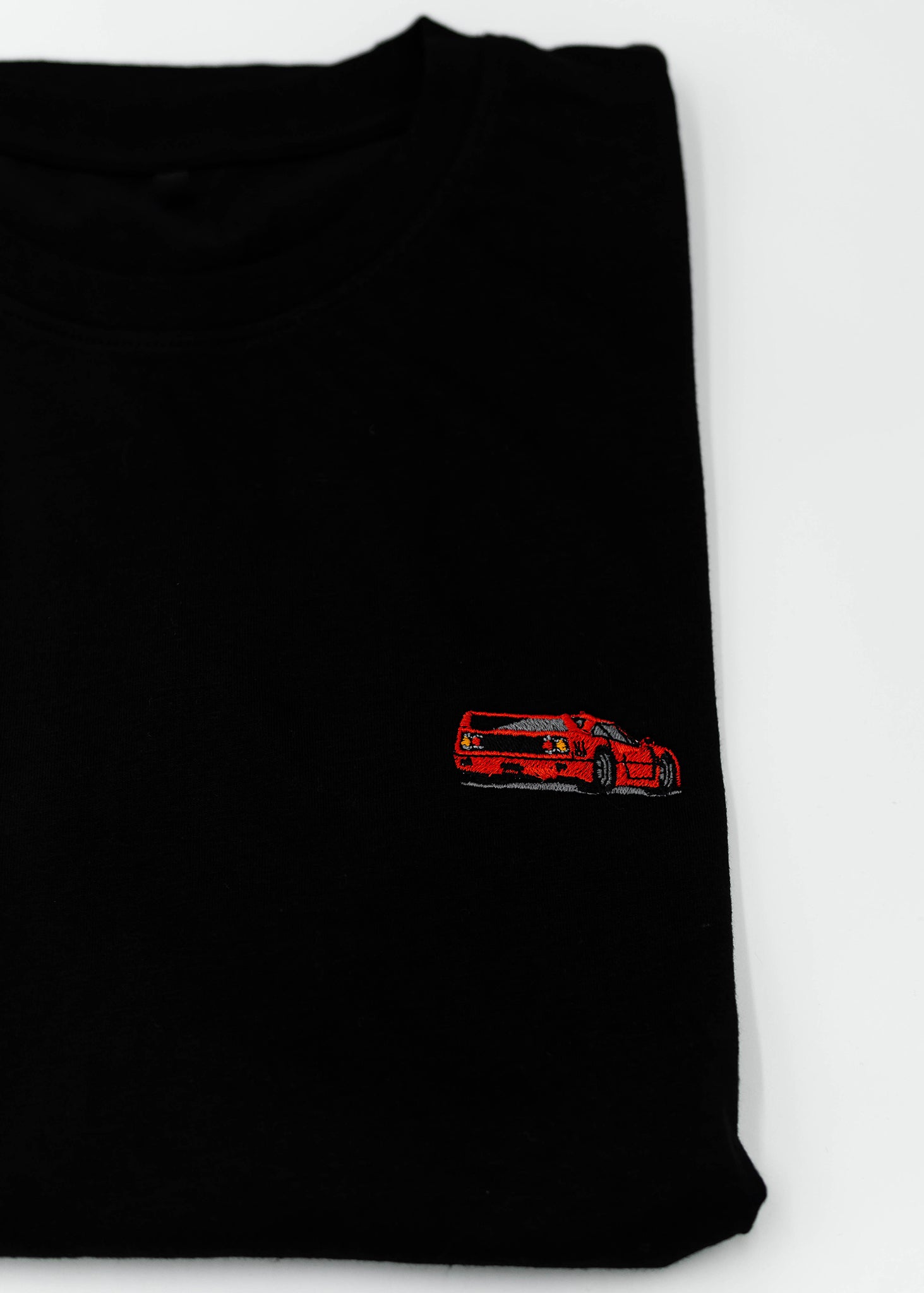 Close up of an embroidered F40 on a black men's cotton t-shirt. Photo shows the high quality detailed embroidery of a red F40. Fabric composition of the shirt is polyester and cotton. The material is very soft, stretchy, and non-transparent. The style of this t-shirt is short sleeve, round bottom, crewneck, with embroidery on the left chest.