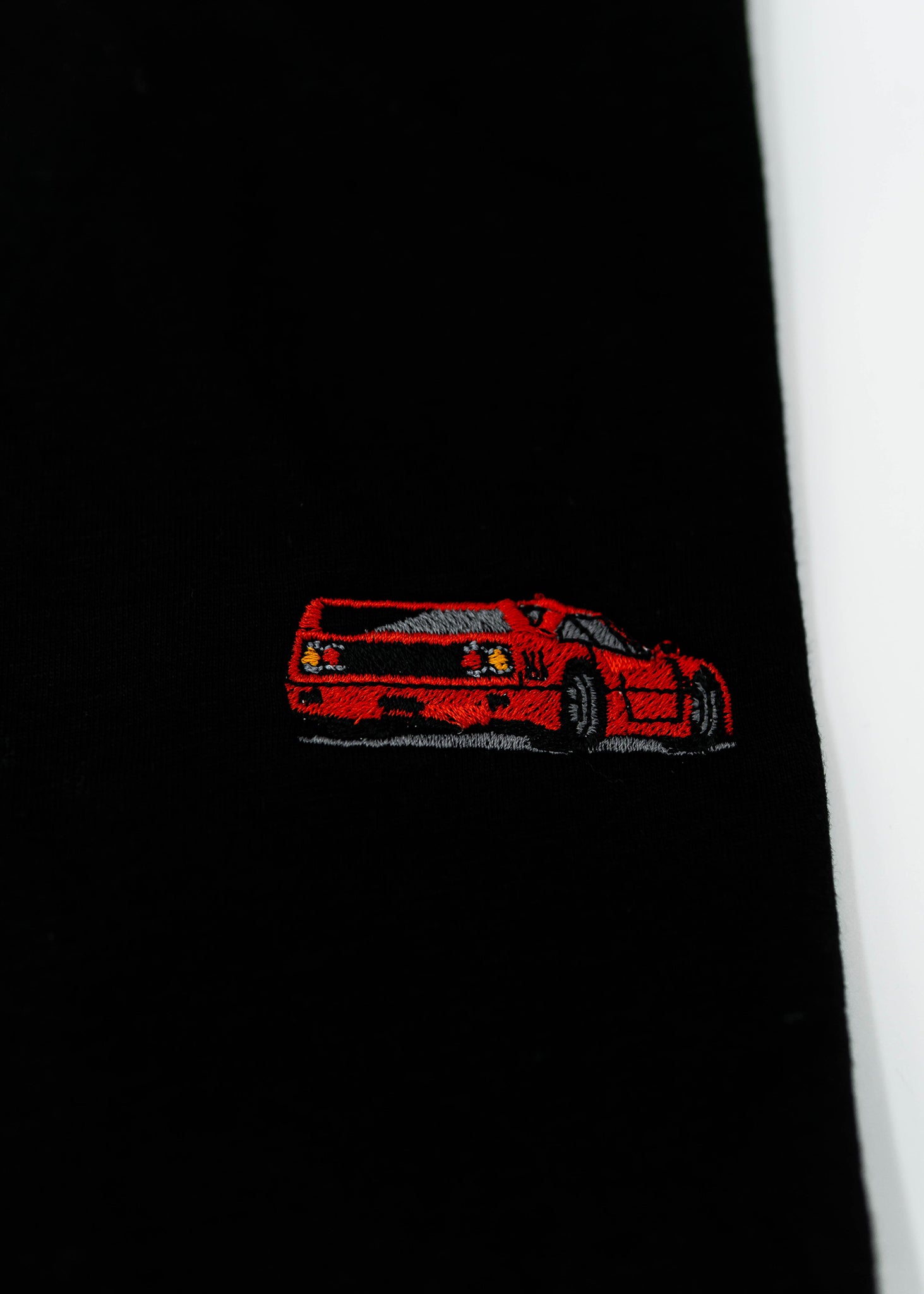 Close up of an embroidered F40 on a black men's cotton t-shirt. Photo shows the high quality detailed embroidery of a red F40. Fabric composition of the shirt is polyester and cotton. The material is very soft, stretchy, and non-transparent. The style of this t-shirt is short sleeve, round bottom, crewneck, with embroidery on the left chest.