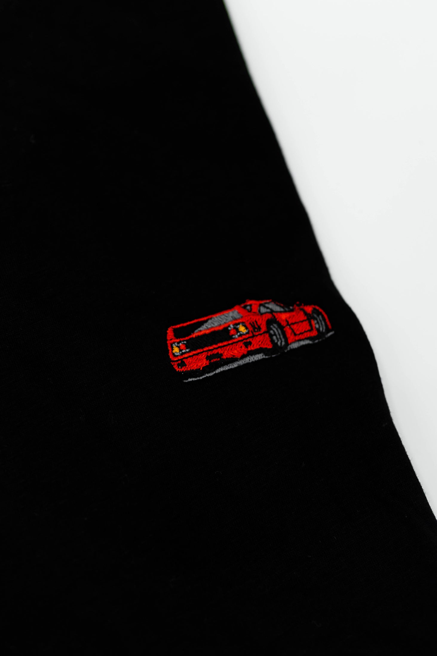 Close up of an embroidered F40 on a black men's cotton t-shirt. Photo shows the high quality detailed embroidery of a red F40. Fabric composition of the shirt is polyester and cotton. The material is very soft, stretchy, and non-transparent. The style of this t-shirt is short sleeve, round bottom, crewneck, with embroidery on the left chest.