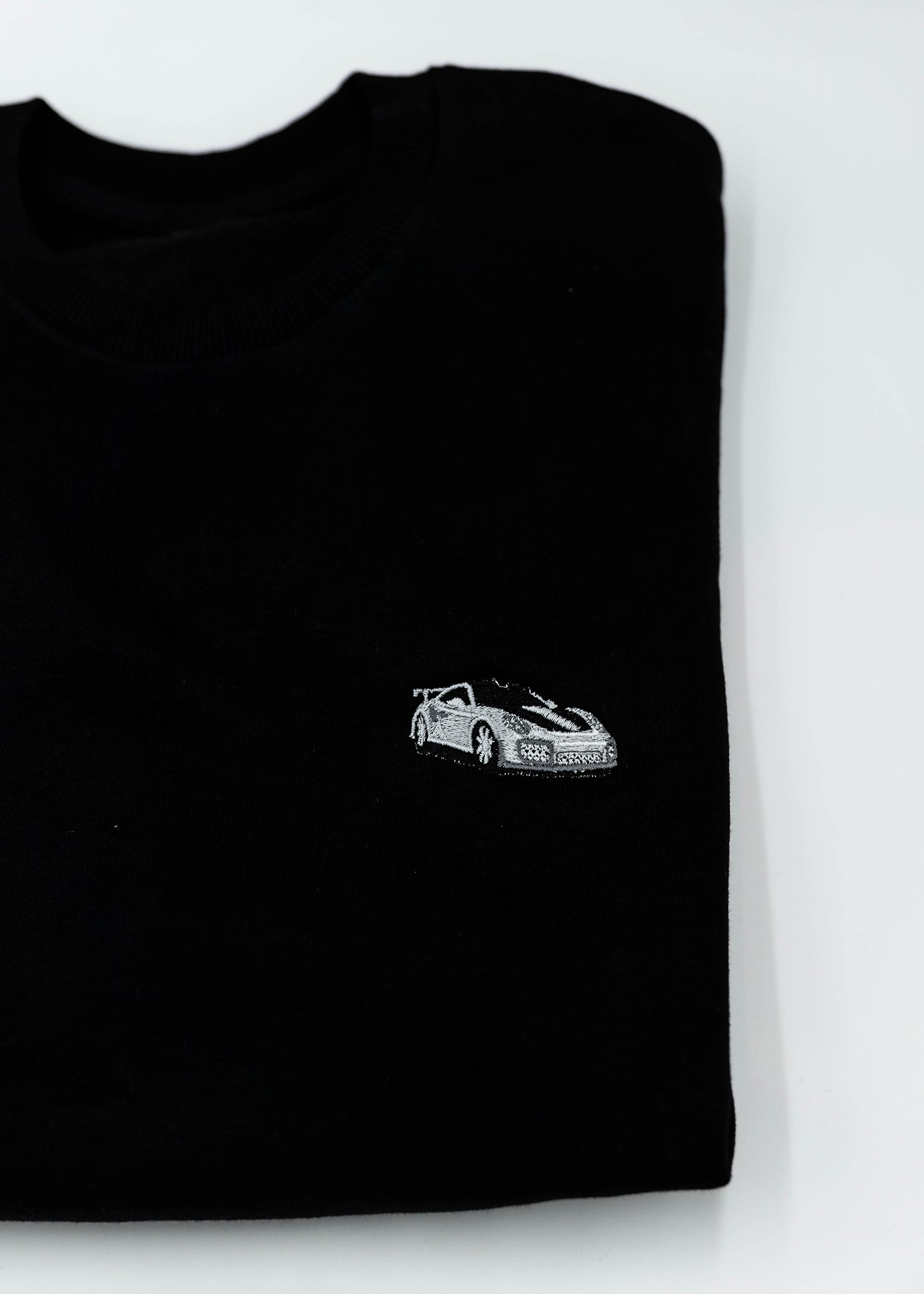 Close up of an embroidered 991.2 GT2 RS on a black men's high quality crewneck sweater. Photo shows the high quality detailed embroidery of a white, silver, and carbon fiber GT2 RS. Fabric composition of the shirt is cotton and polyester. The material is very soft, stretchy, and non-transparent. The style of this sweater is a crewneck, long sleeve, elastic bottom, with embroidery on the left chest.