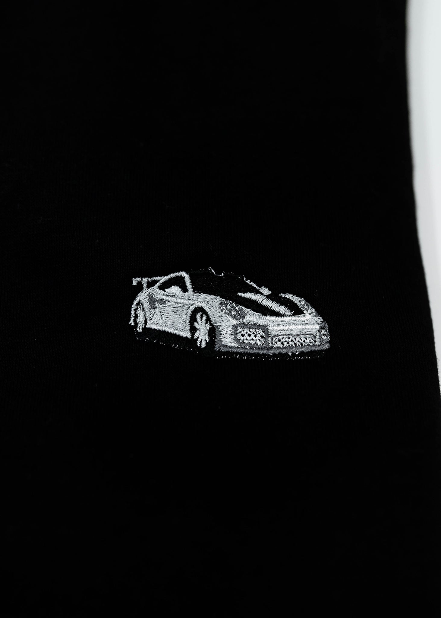 Close up of an embroidered 991.2 GT2 RS on a black men's high quality crewneck sweater. Photo shows the high quality detailed embroidery of a white, silver, and carbon fiber GT2 RS. Fabric composition of the shirt is cotton and polyester. The material is very soft, stretchy, and non-transparent. The style of this sweater is a crewneck, long sleeve, elastic bottom, with embroidery on the left chest.