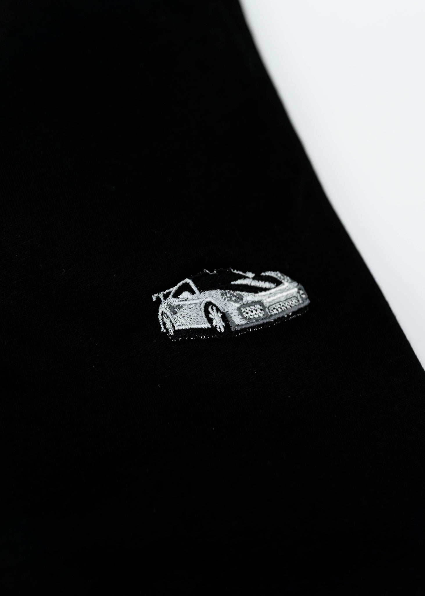Close up of an embroidered 991.2 GT2 RS on a black men's high quality crewneck sweater. Photo shows the high quality detailed embroidery of a white, silver, and carbon fiber GT2 RS. Fabric composition of the shirt is cotton and polyester. The material is very soft, stretchy, and non-transparent. The style of this sweater is a crewneck, long sleeve, elastic bottom, with embroidery on the left chest.