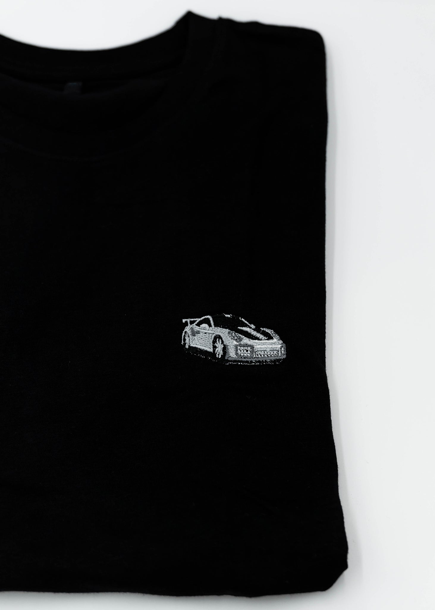 Close up of an embroidered 991.2 GT2 RS on a black men's cotton t-shirt. Photo shows the high quality detailed embroidery of a white, silver, and carbon fiber GT2 RS. Fabric composition of the shirt is polyester and cotton. The material is very soft, stretchy, and non-transparent. The style of this t-shirt is short sleeve, round bottom, crewneck, with embroidery on the left chest.