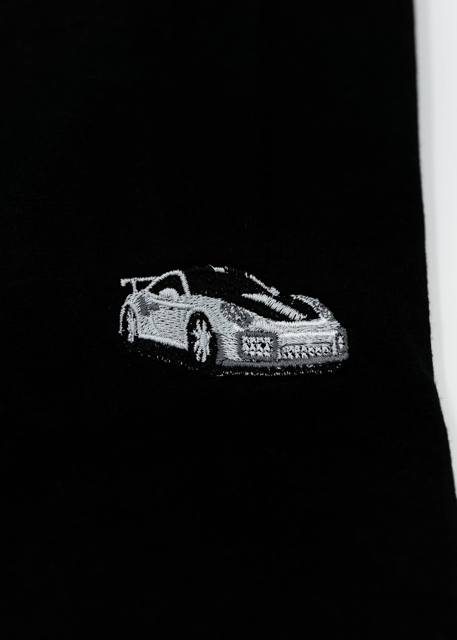 Close up of an embroidered 991.2 GT2 RS on a black men's cotton t-shirt. Photo shows the high quality detailed embroidery of a white, silver, and carbon fiber GT2 RS. Fabric composition of the shirt is polyester and cotton. The material is very soft, stretchy, and non-transparent. The style of this t-shirt is short sleeve, round bottom, crewneck, with embroidery on the left chest.