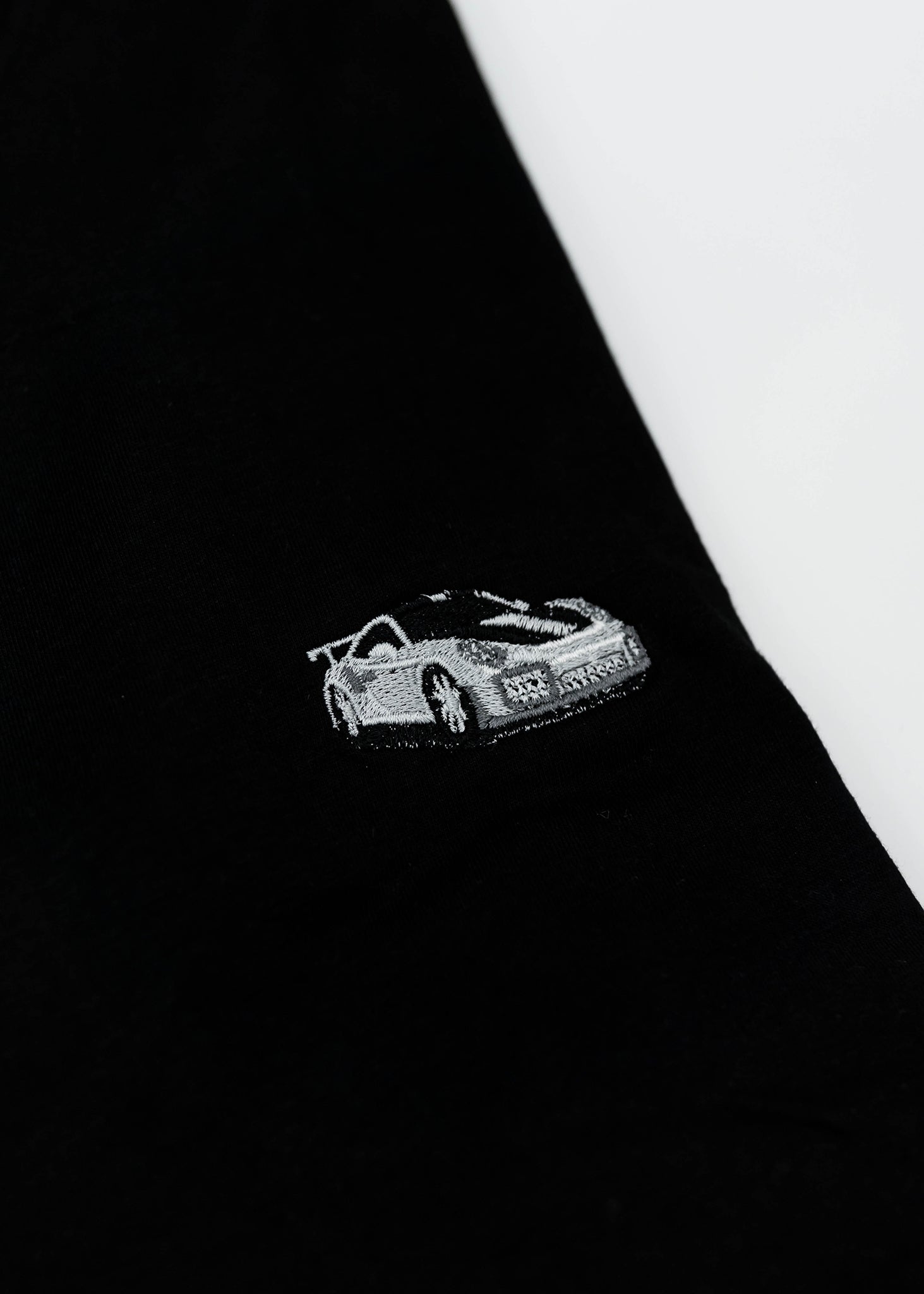 Close up of an embroidered 991.2 GT2 RS on a black men's cotton t-shirt. Photo shows the high quality detailed embroidery of a white, silver, and carbon fiber GT2 RS. Fabric composition of the shirt is polyester and cotton. The material is very soft, stretchy, and non-transparent. The style of this t-shirt is short sleeve, round bottom, crewneck, with embroidery on the left chest.