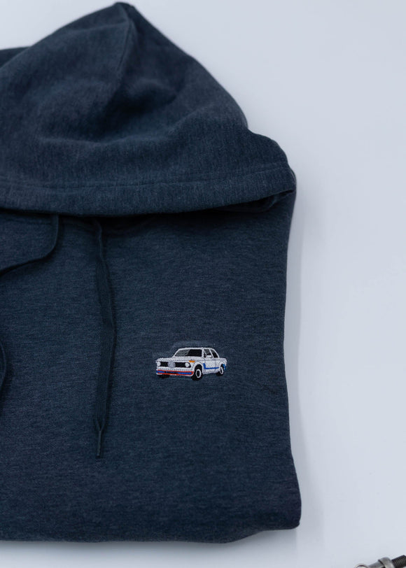 A dark blue BMW unisex hoodie for men and women. Photo is a close up view of the sweater with an embroidered BMW 2002 Turbo. Fabric composition is cotton, polyester, and rayon. The material is very soft, stretchy, and non-transparent. The style of this hoodie is long sleeve, crewneck with a hood, hooded, with embroidery on the left chest.