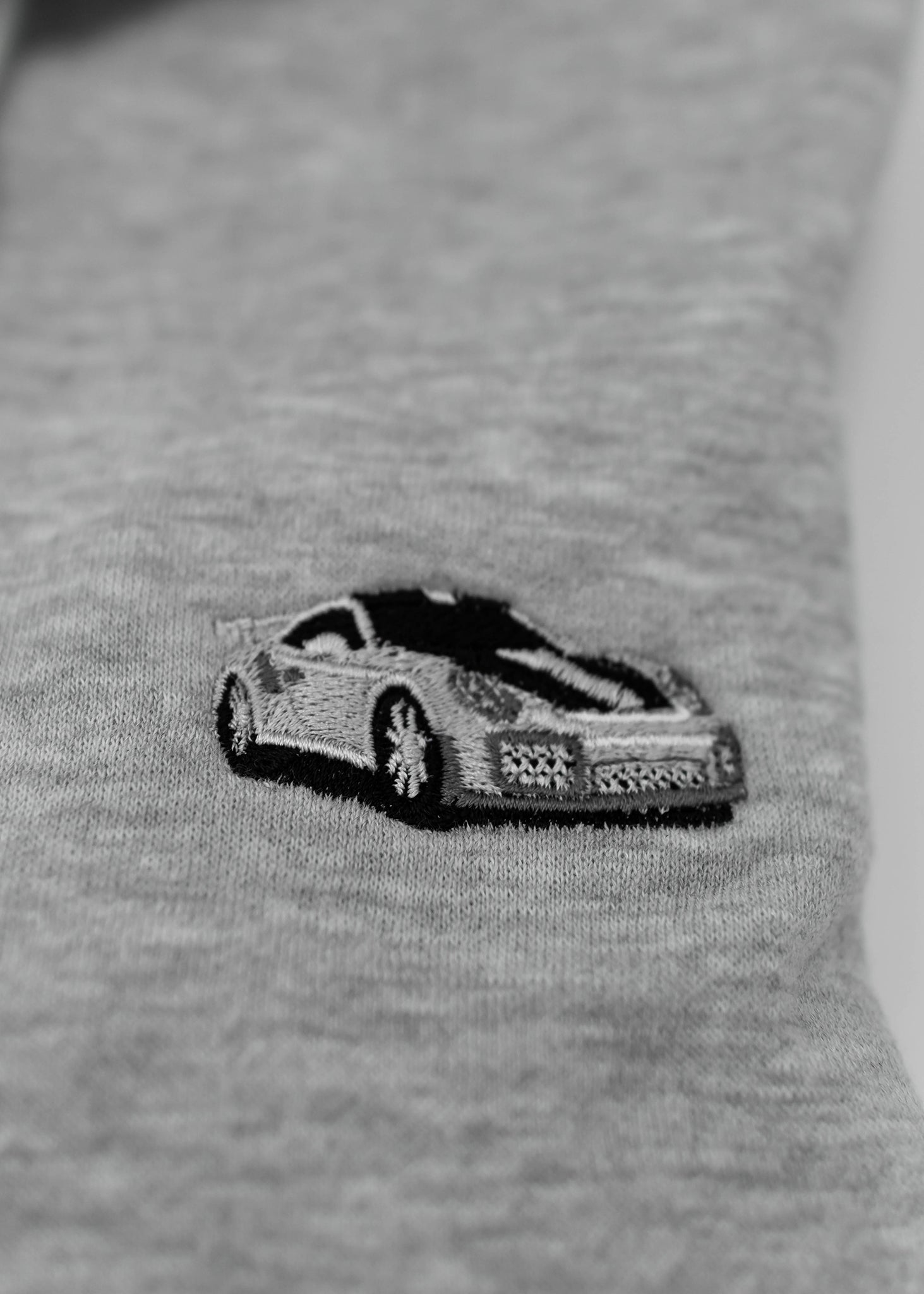 Close up of an embroidered 991.2 GT2 RS on a women's high quality cropped grey hoodie. Photo shows the detailed embroidery of a white, silver, and carbon fiber GT2 RS. Fabric composition of this cropped sweater is polyester and cotton. The material is very soft, stretchy, and non-transparent. The style of this crop hoodie is a crewneck, drawstring hoodie, hooded, long sleeve, cropped, with embroidery on the left chest.