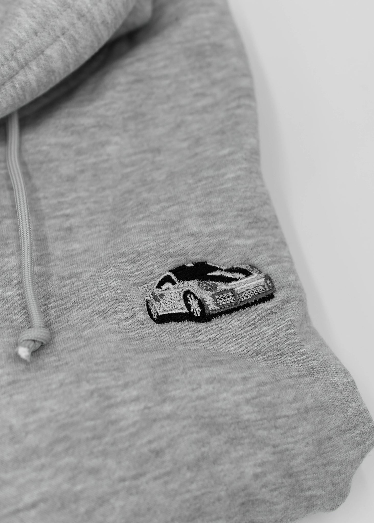 Close up of an embroidered 991.2 GT2 RS on a women's high quality cropped grey hoodie. Photo shows the detailed embroidery of a white, silver, and carbon fiber GT2 RS. Fabric composition of this cropped sweater is polyester and cotton. The material is very soft, stretchy, and non-transparent. The style of this crop hoodie is a crewneck, drawstring hoodie, hooded, long sleeve, cropped, with embroidery on the left chest.
