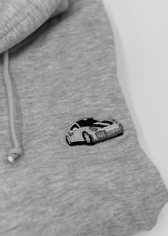 Close up of an embroidered 991.2 GT2 RS on a women's high quality cropped grey hoodie. Photo shows the detailed embroidery of a white, silver, and carbon fiber GT2 RS. Fabric composition of this cropped sweater is polyester and cotton. The material is very soft, stretchy, and non-transparent. The style of this crop hoodie is a crewneck, drawstring hoodie, hooded, long sleeve, cropped, with embroidery on the left chest.