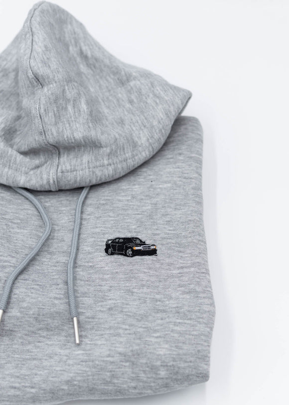 A grey Mercedes-Benz cropped hoodie for women. Photo is a close up view of the cropped sweater with an embroidered W201 190E 2.5-16 Evo II. Fabric composition is 100% cotton. The material is soft, comfortable, breathable, and non-transparent. The style of this crop hoodie is long sleeve, crewneck with a hood, hooded, with embroidery on the chest.