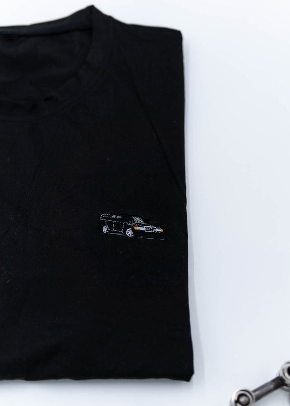 A black Mercedes-Benz t-shirt for men. Photo is a close up of the shirt with an embroidered black W201 190E Evo II. Fabric composition is a polyester. The material is very soft, stretchy, non-transparent. The style of this shirt is short sleeve, with a crewneck neckline.