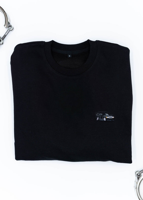 A black Mercedes-Benz crewneck sweater for men. Photo is a close up of the sweater with an embroidered Mercedes-Benz W201 190E 2.5-16 Evo II. Fabric is composed of high quality 80% cotton, and 20% polyester and fits to size. The style is long sleeve, crew neck, and embroidery on left chest.