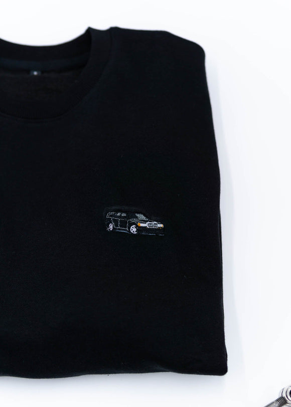 A black Mercedes-Benz crewneck sweater for men. Photo is a close up of the sweater with an embroidered Mercedes-Benz W201 190E 2.5-16 Evo II. Fabric is composed of high quality 80% cotton, and 20% polyester and fits to size. The style is long sleeve, crew neck, and embroidery on left chest.