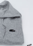A grey Mercedes-Benz unisex hoodie for men and women. Photo is a close up view of the sweater with an embroidered Mercedes-Benz W201 190E 2.5-16 Evo II. Fabric composition is cotton, polyester, and rayon. The material is very soft, stretchy, and non-transparent. The style of this hoodie is long sleeve, crewneck with a hood, hooded, with embroidery on the left chest.