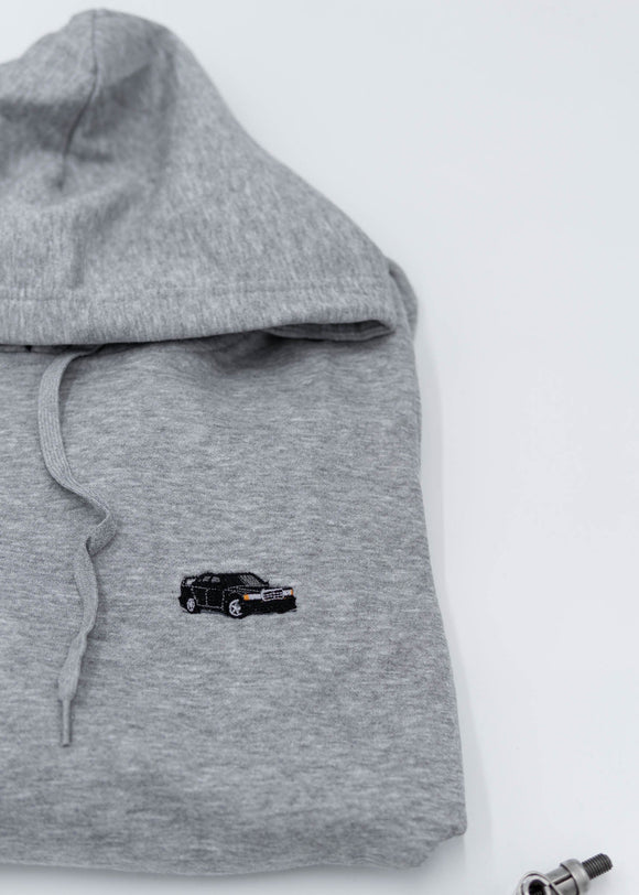 A grey Mercedes-Benz unisex hoodie for men and women. Photo is a close up view of the sweater with an embroidered Mercedes-Benz W201 190E 2.5-16 Evo II. Fabric composition is cotton, polyester, and rayon. The material is very soft, stretchy, and non-transparent. The style of this hoodie is long sleeve, crewneck with a hood, hooded, with embroidery on the left chest.