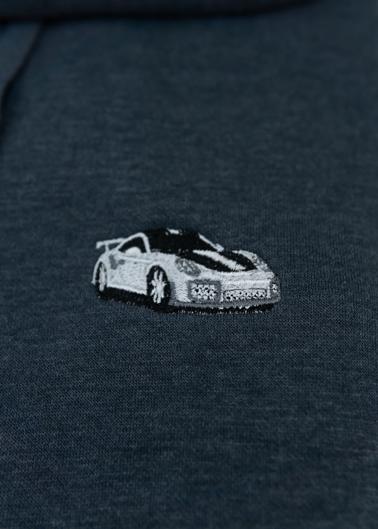 Close up of an embroidered GT2 RS on a navy blue unisex hoodie for men and women. Photo shows the high quality detailed embroidery of a white, silver, carbon fiber GT2 RS on the left chest. Fabric composition of the sweater is cotton, polyester, and rayon. The material is very soft, stretchy, and non-transparent. The style of this hoodie is long sleeve, crewneck with a hood, hooded, with embroidery on the left chest.