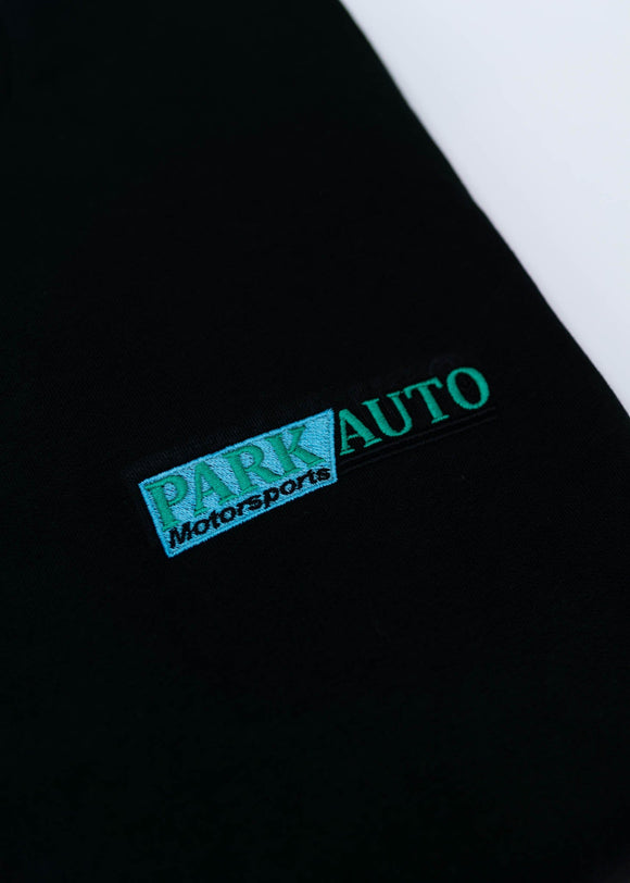 A black Park Auto Motorsports crewneck sweater for men. Photo is a close up of the sweater with an embroidered logo. Fabric is composed of high quality 80% cotton, and 20% polyester and fits to size. The style is long sleeve, crew neck, and embroidery on left chest.