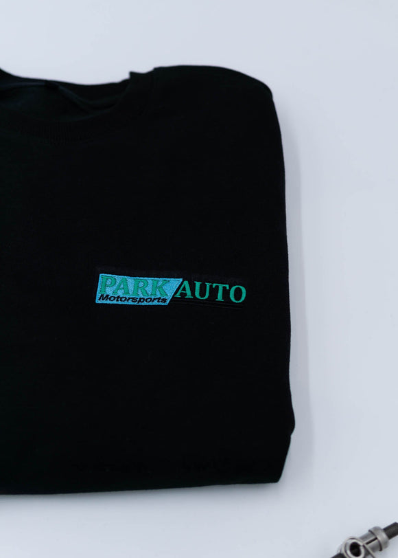 A black Park Auto Motorsports crewneck sweater for men. Photo is a close up of the sweater with an embroidered logo. Fabric is composed of high quality 80% cotton, and 20% polyester and fits to size. The style is long sleeve, crew neck, and embroidery on left chest.