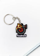 A pizzabrand pizza and turbo keychain. Made of rubber and stainless steel. Photo is of a close up of the pizza melting on a turbo with the brand name.