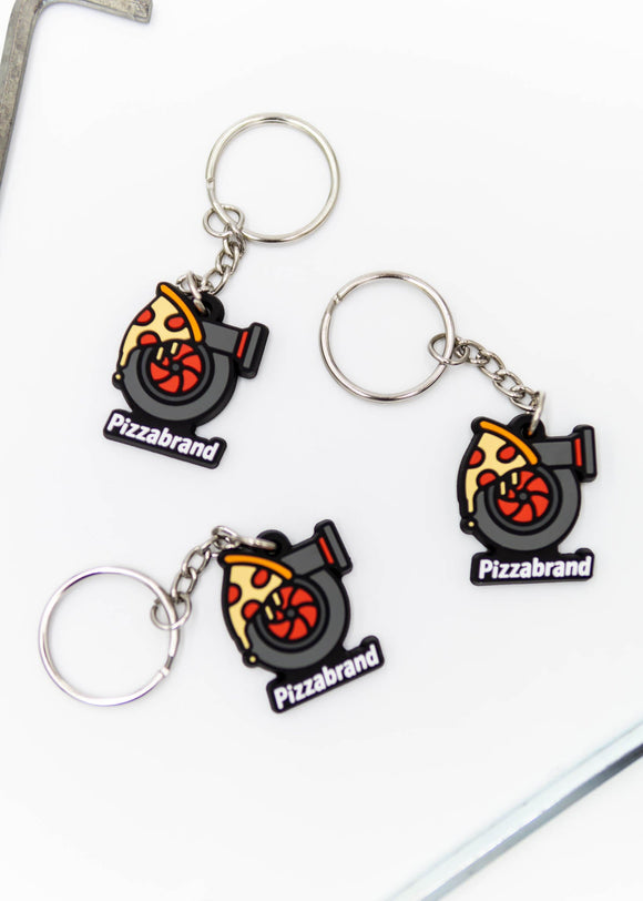 A pizzabrand pizza and turbo keychain. Made of rubber and stainless steel. Photo is of a close up of 3 keychains. The pizza melting on a turbo with the brand name.