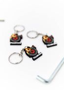 A pizzabrand pizza and turbo keychain. Made of rubber and stainless steel. Photo is of a close up of 3 keychains. The pizza melting on a turbo with the brand name.