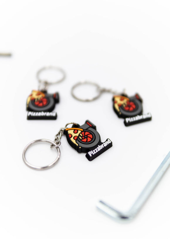A pizzabrand pizza and turbo keychain. Made of rubber and stainless steel. Photo is of a close up of 3 keychains. The pizza melting on a turbo with the brand name.