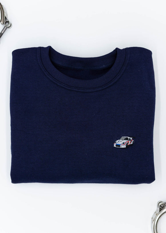 A navy blue Porsche race car crewneck sweater for men. Photo is a front view of the sweater with an embroidered Martini R13 Porsche 911 Carrera RSR 2.1 Turbo . Fabric is 100% cotton and high quality and fits to size. The style is long sleeve, crew neck, and embroidery on left chest.