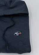 A dark grey Porsche racing unisex hoodie for men and women. Photo is a close up of the sweater with an embroidered Martini R13 Porsche 911 Carrera RSR 2.1 Turbo. Fabric composition is cotton, polyester, and rayon. The material is very soft, stretchy, and non-transparent. The style of this hoodie is long sleeve, crewneck with a hood, hooded, with embroidery on the left chest.