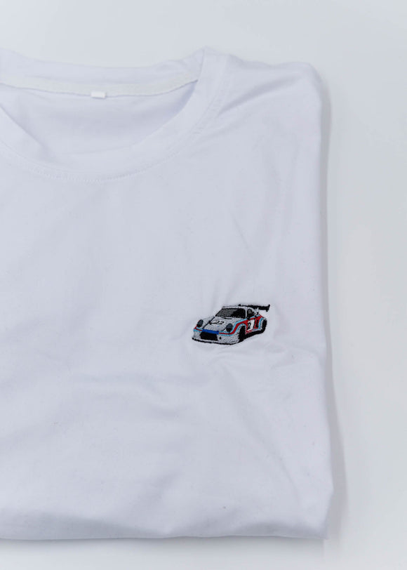 A white Porsche T-Shirt for men. Photo is a close up of the shirt with an embroidered Martini R13 Porsche 911 Carrera RSR 2.1 Turbo. Fabric composition is 100% polyester. The material is very stretchy, soft, comfortable, breathable, and non-transparent. The style of this shirt is short sleeve, with a crewneck neckline.