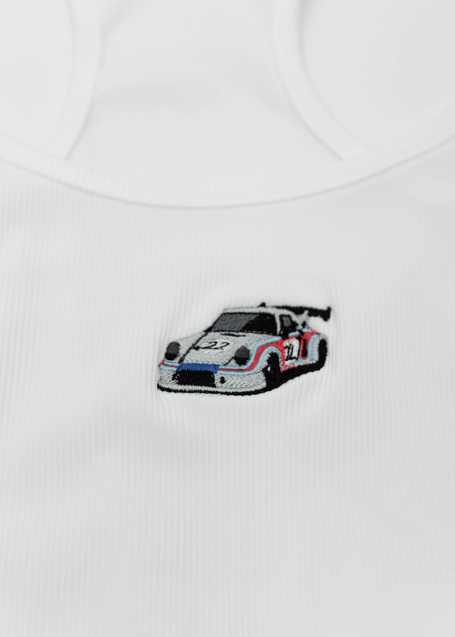 Close up of an embroidered R13 1974 911 RSR Turbo on a women's high quality ribbed racer back crop top. Photo shows the detailed embroidery of a R13 1974 911 RSR Turbo. Fabric composition of this tee is 95% polyester, and 5% elastane. The material is very stretchy, and form fitting. The style of this shirt is scoop neck, sleeveless, cropped at the waist, with embroidery in the middle.