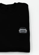 Close up of an embroidered 8V RS3 on a black men's high quality crewneck sweater. Photo shows the high quality detailed embroidery of a nardo grey 8V RS3. Fabric composition of the shirt is cotton and polyester. The material is very soft, stretchy, and non-transparent. The style of this sweater is a crewneck, long sleeve, elastic bottom, with embroidery on the left chest.