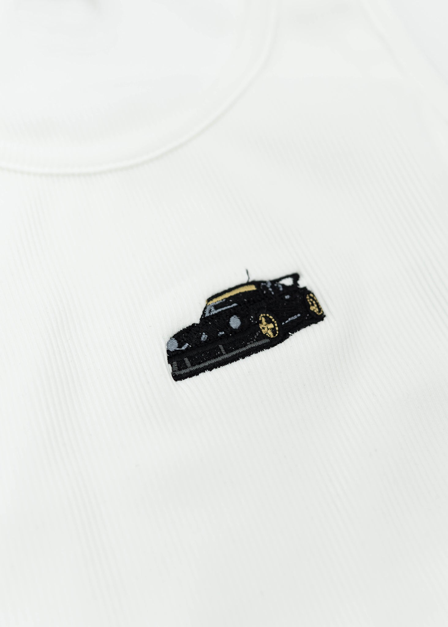 Close up of an embroidered RWB 930 911 Turbo - Akira Nakai "Stella Artois" on a women's high quality ribbed racer back crop top. Photo shows the detailed embroidery of a RWB 930 911 Turbo. Fabric composition of this tee is 95% polyester, and 5% elastane. The material is very stretchy, and form fitting. The style of this shirt is scoop neck, sleeveless, cropped at the waist, with embroidery in the middle.