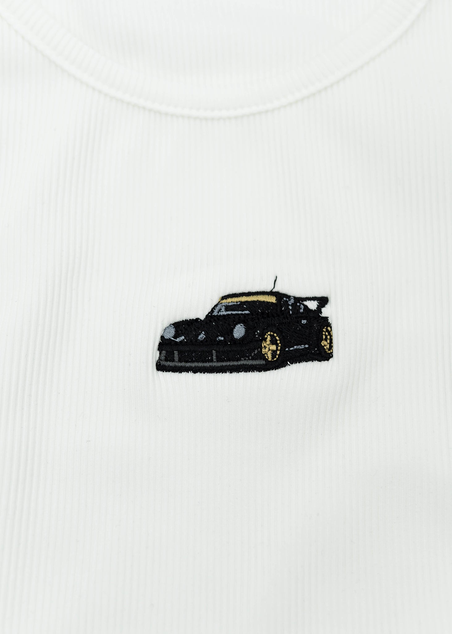 Close up of an embroidered RWB 930 911 Turbo - Akira Nakai "Stella Artois" on a women's high quality ribbed racer back crop top. Photo shows the detailed embroidery of a RWB 930 911 Turbo. Fabric composition of this tee is 95% polyester, and 5% elastane. The material is very stretchy, and form fitting. The style of this shirt is scoop neck, sleeveless, cropped at the waist, with embroidery in the middle.