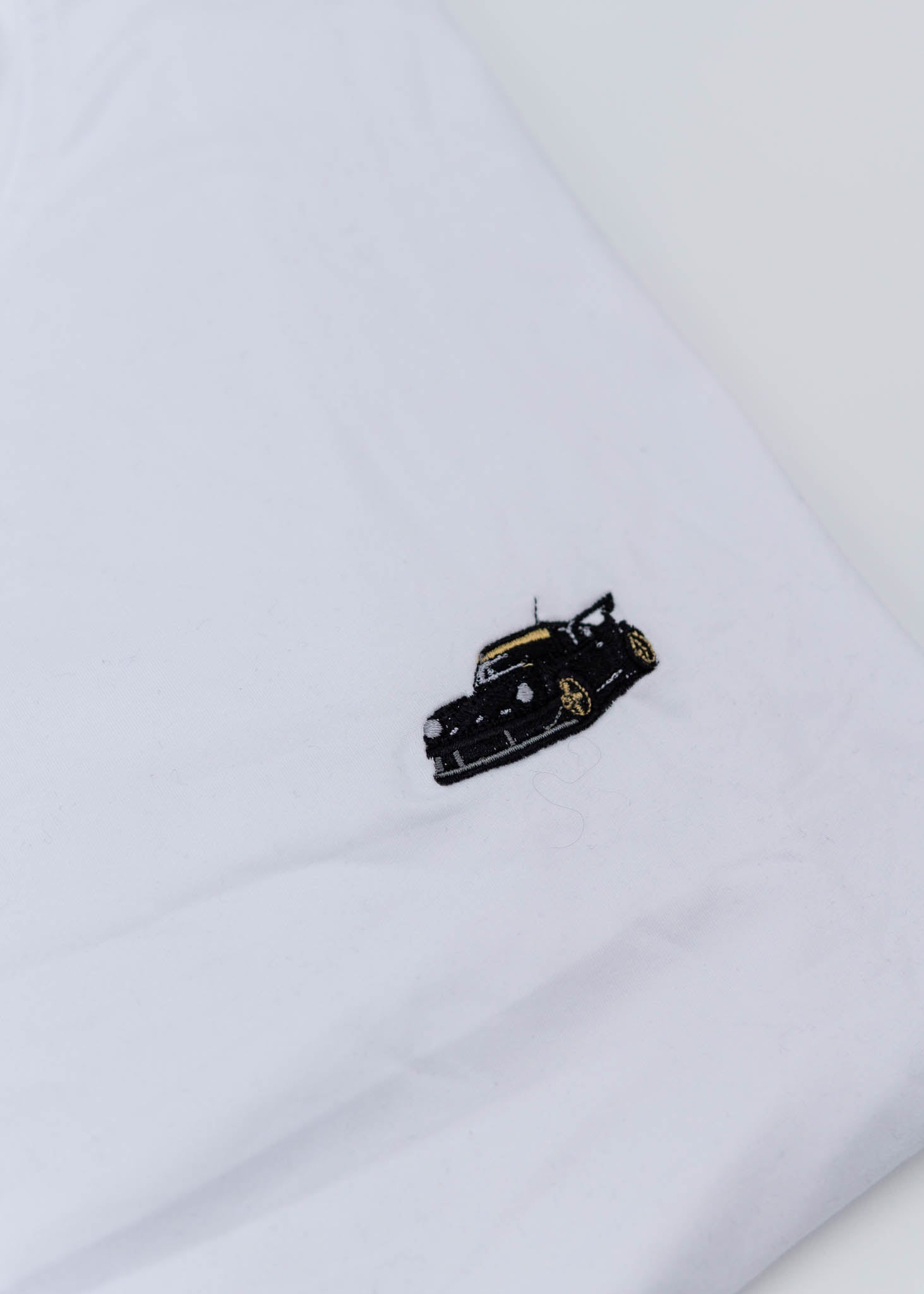 A white Porsche T-Shirt for men. Photo is a close up of the shirt with an embroidered RWB Porsche 930 911 Turbo Stella Artois. Fabric composition is 100% polyester. The material is very stretchy, soft, comfortable, breathable, and non-transparent. The style of this shirt is short sleeve, with a crewneck neckline.